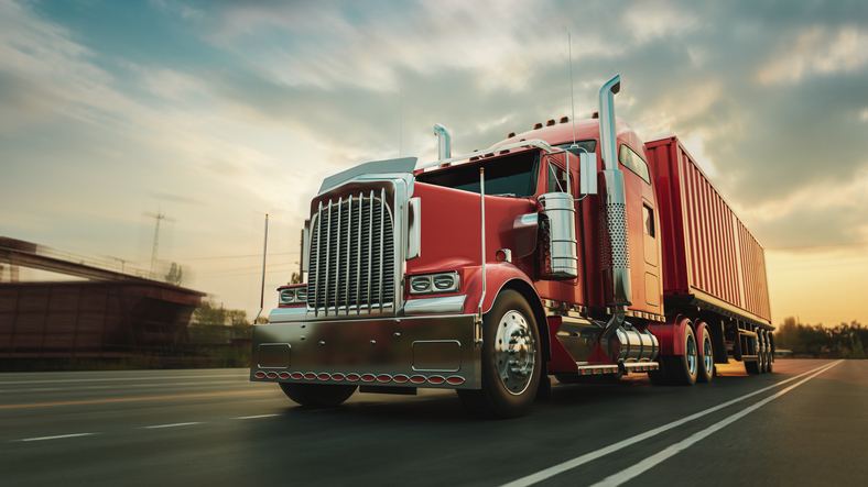 A large red semi-truck traveling down the highway with a blurred evening background