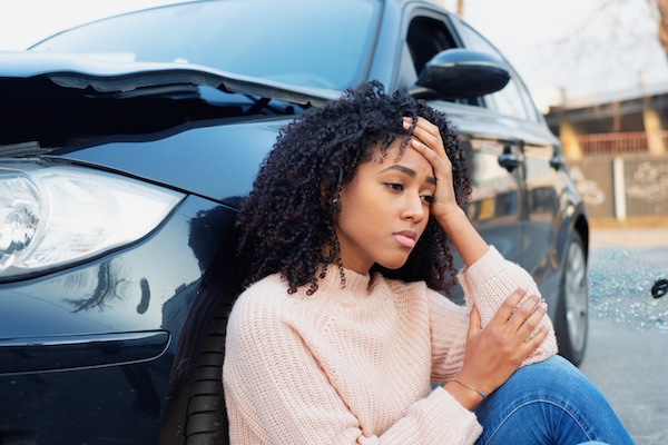 distraught woman sits by her damaged car after an accident