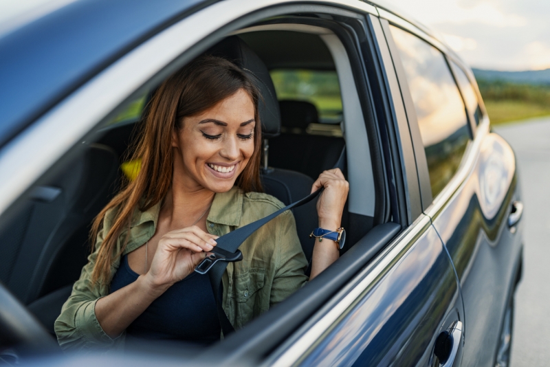 A young woman smiles and leans over to buckle her seat belt