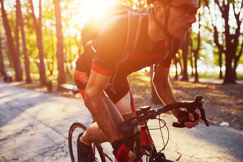 Road biker on a paved road in the sunset wearing full biking gear and helmet