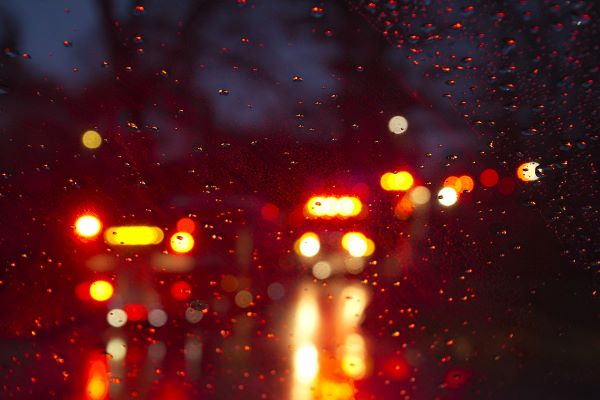 Blurry view of emergency vehicles and brake lights through a rainy windshield