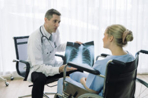 A doctor is seated and showing a patient in a wheelchair an x-ray of her chest