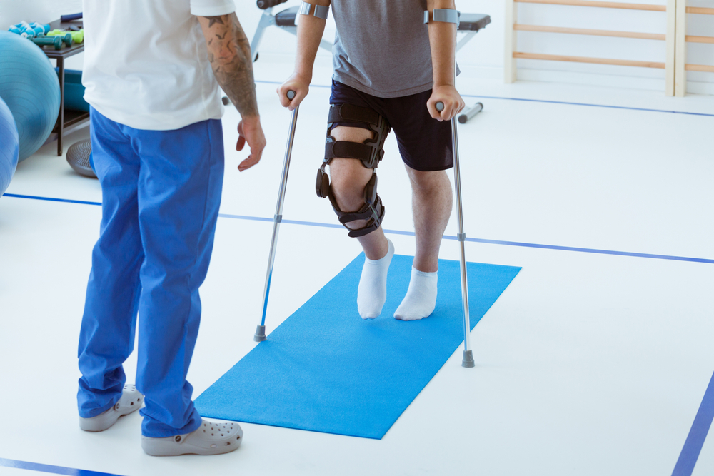A close up of a man with a leg brace performing physical therapy with an assistant