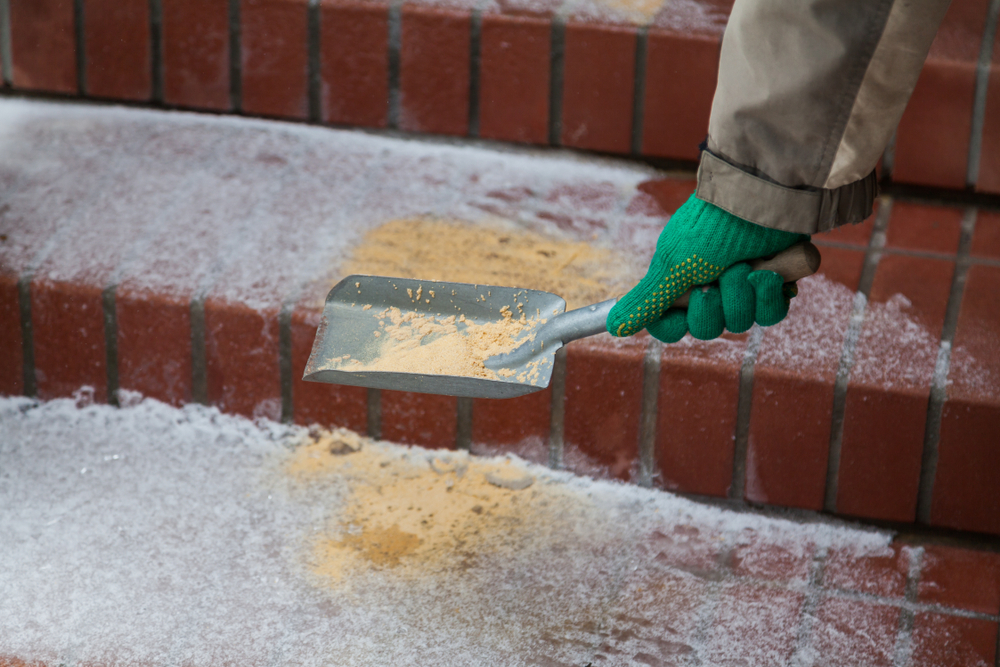 A close up of snowy outdoor stairs and a person's gloved hand sprinkling sand on the steps for traction