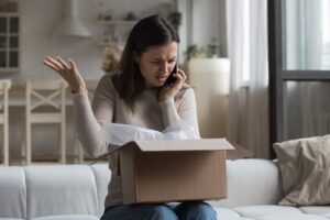 Woman sit on sofa open parcel box looks inside check purchased damaged items