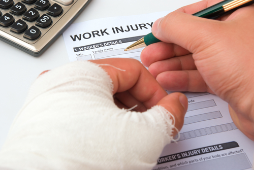 filling up a work injury claim form with a wrapped hand filling up a work injury claim form with a wrapped hand